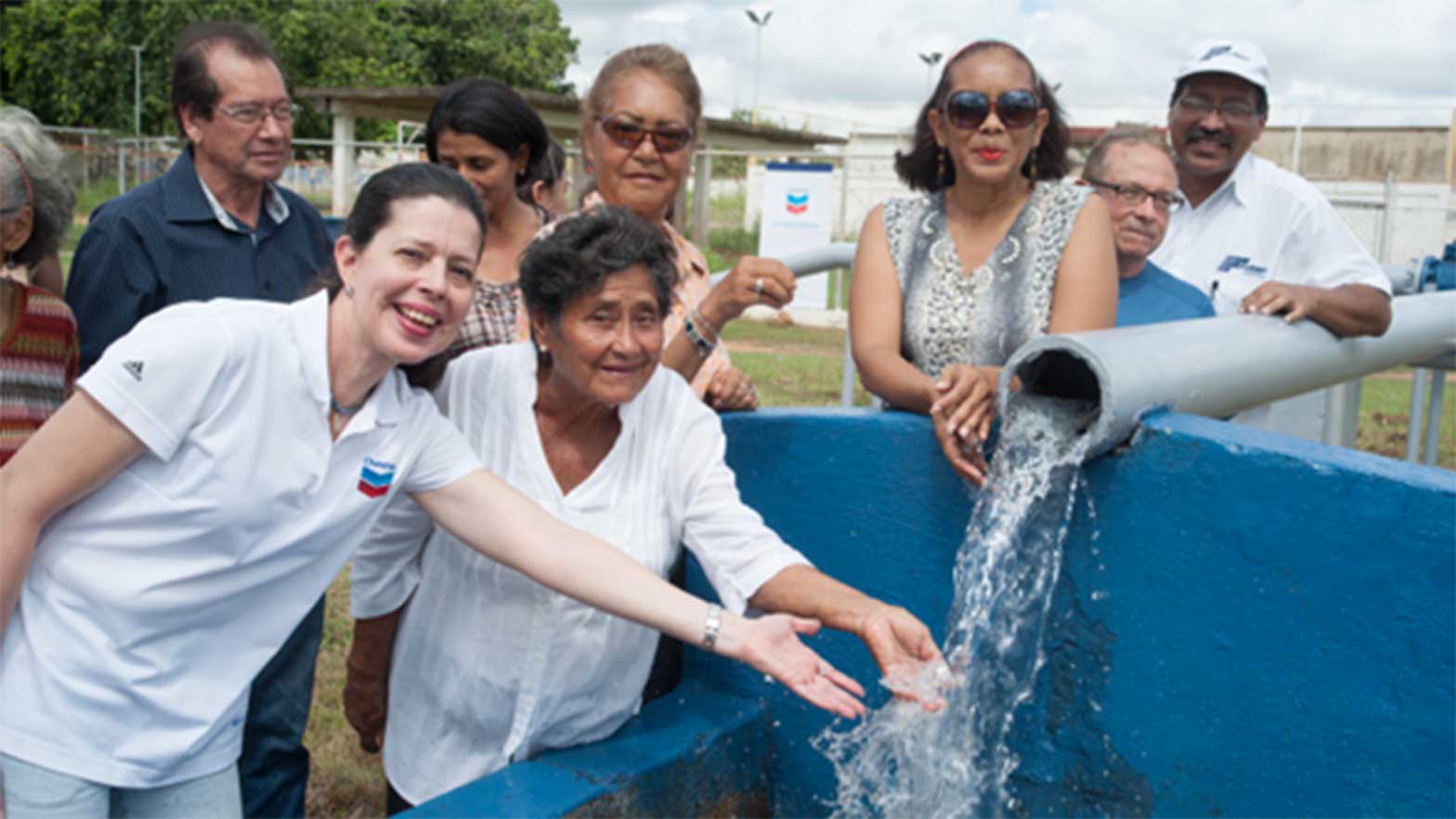 a group of smiling people touching water pouring out of a pipe