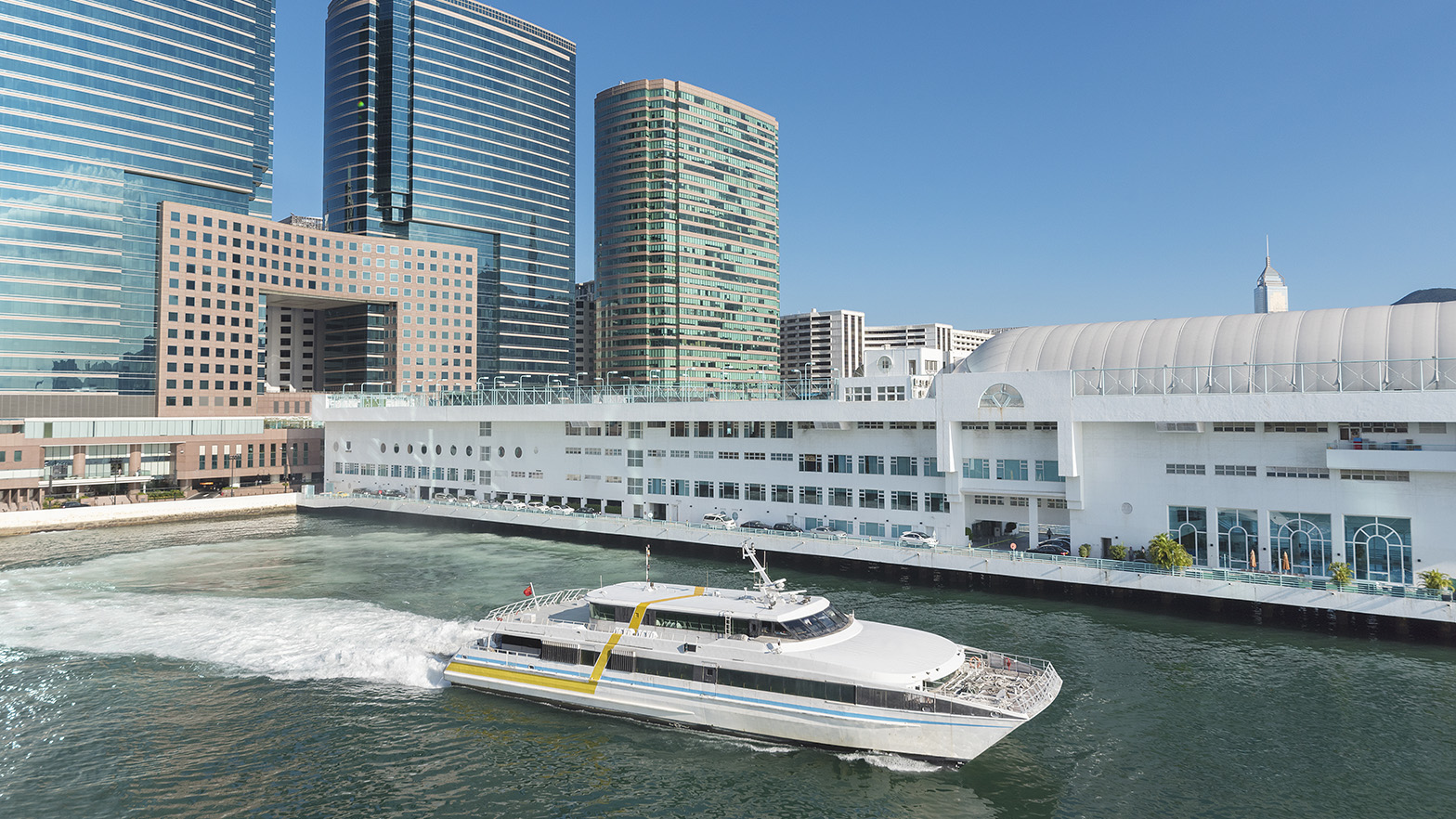 A yacht passing along a riverway near a city with skyscrapers